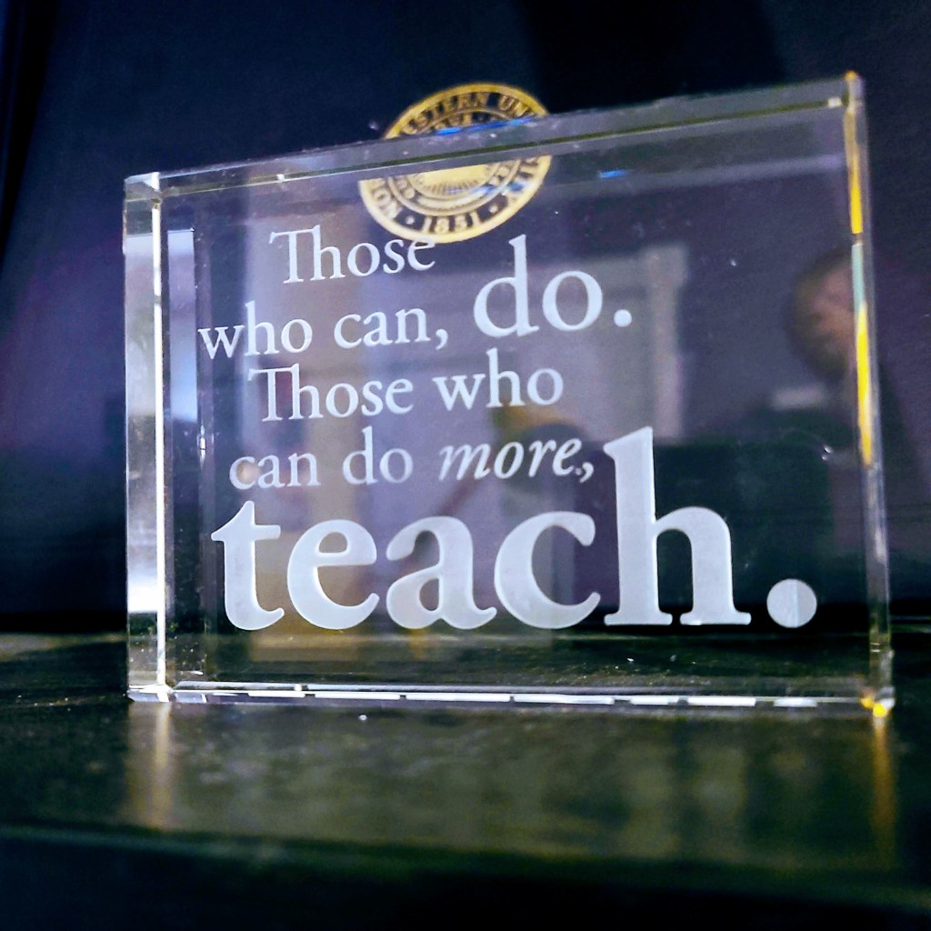 Placard saying "Those who can, do. Those who can do more, teach."